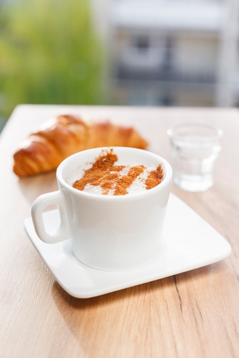 flat lay photography of white mug on white saucer plate and croshan bread